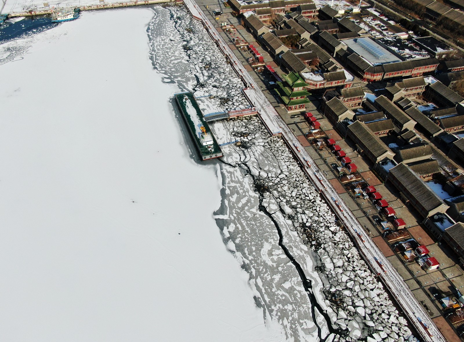 1月17日，新区迎来2024年首场降雪。18日清晨，位于滨海新区中新天津生态城中心渔港的鲤鱼门周围覆盖了薄薄的白雪，雪后独具特色的仿古建筑与海边的冰上覆盖的皑皑白雪，宛如一幅美丽的画卷。